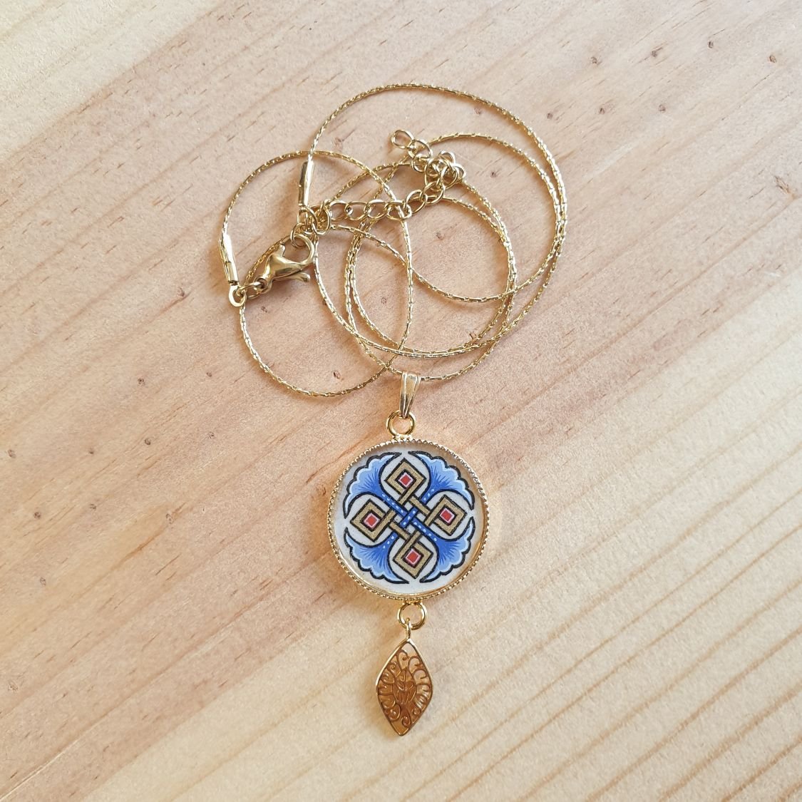Halshanger verlicht met blauwe palmetten, goud en rood vlechtwerk aan gouden ketting