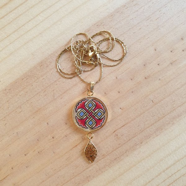 Halshanger verlicht met blauwe palmetten, goud en rood vlechtwerk aan gouden ketting