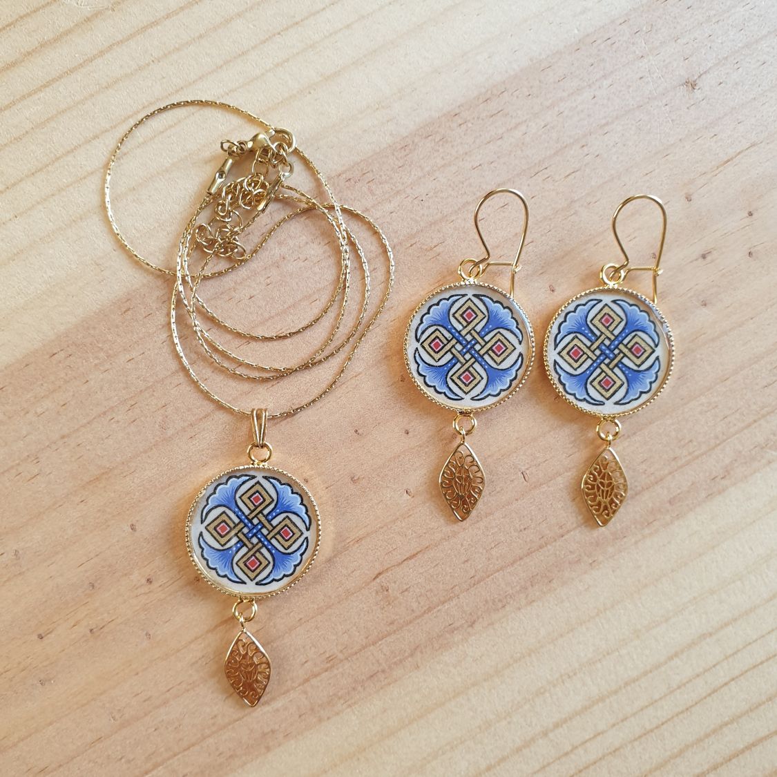 Halshanger verlicht met blauwe palmetten, goud en rood vlechtwerk aan gouden ketting