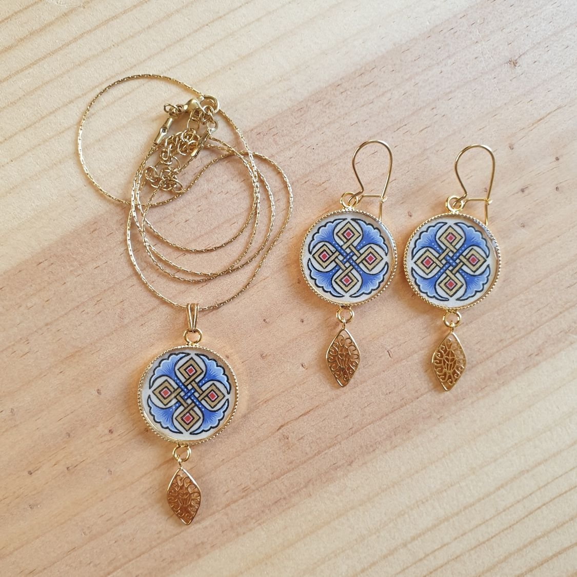 Halshanger verlicht met blauwe palmetten, goud en rood vlechtwerk aan gouden ketting