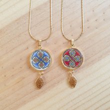 Halshanger verlicht met blauwe palmetten, goud en rood vlechtwerk aan gouden ketting